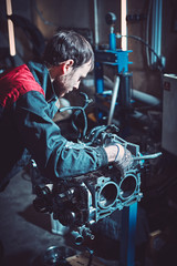 Fototapeta na wymiar The young auto mechanic dismantles the opposing engine.