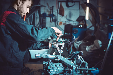 The young auto mechanic dismantles the opposing engine. - obrazy, fototapety, plakaty
