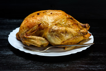 roast chicken on a white plate, on a black wooden background