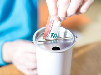 Spenden, 10 Euro werden in eine Spendedose gesteckt