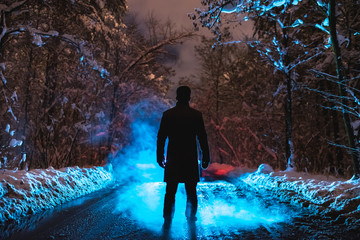 The man stand near the blue smoke in the winter forest. evening night time