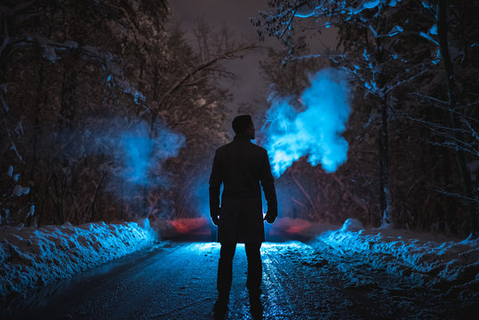 The man smoke on the snowy road in the dark forest. evening night time