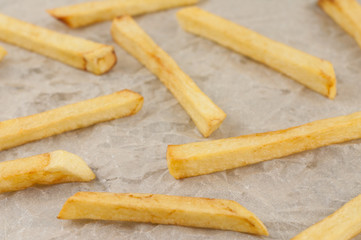 Scattered lot of sticks of tasty french fries on gray crumpled paper