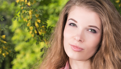 Horizontal closeup portrait of a beautiful young woman with her hair in nature. Long natural hair, light makeup, pink shirt