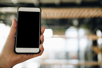 mockup image of hand holding smartphone in cafe restaurant. mobile phone with blank white screen in coffee shop.