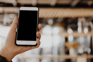 mockup image of hand holding smartphone in cafe restaurant. mobile phone with blank white screen in coffee shop.