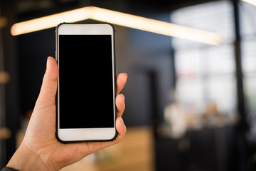 mockup image of hand holding smartphone in cafe restaurant. mobile phone with blank white screen in coffee shop.