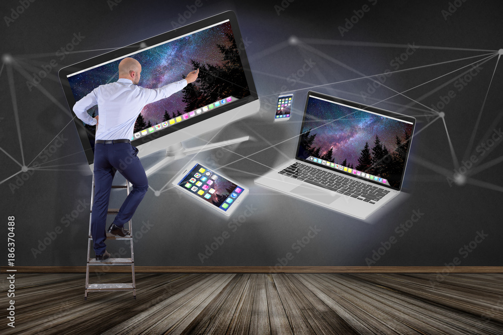Poster businessman in front of a wall with devices like smartphone, tablet or computer flying over connecti