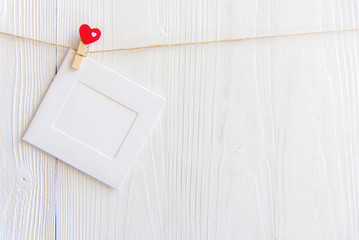 Blank instant photo frame and red  heart hanging on the clothesline. On white old wood background.  Valentine Concept..