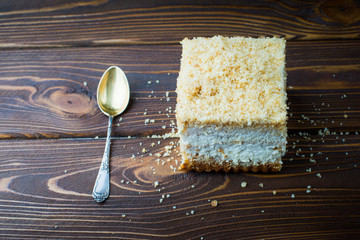Delicious piece of cake with a spoon on a wooden table. Crumbs on a wooden table with a cake.