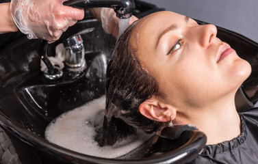 Close up profile view of young woman having hair washed by stylist after dyeing
