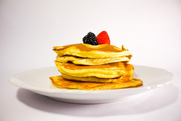 pancakes on a white plate with raspberries and strawberry on top