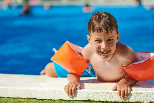 Smiling Caucasian boy getting out from the swimming pool through its side.