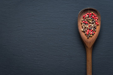 Wooden spoon filled with dried peppercorn on black background. Top view, copy space.