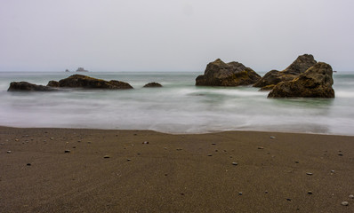 Fototapeta na wymiar Sand and Smooth Waves Among Rocks