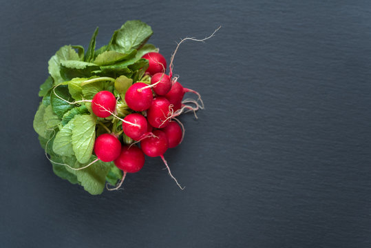 Bunch of radish with leaves on black background. Top view, copy space.
