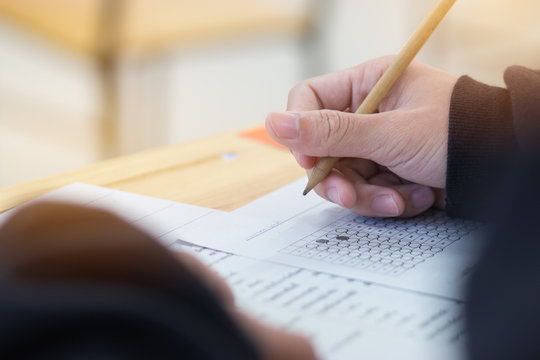 High School Or University Student Hands Taking Exams, Writing Examination On Paper Answer Sheet Optical Form Of Standardized Test On Desk Doing Final Exam In Classroom. Education  Literacy Concept.