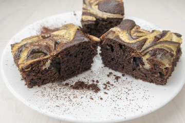 Three mouth-watering chocolate cakes are located on a white plate that is light on a wooden background.