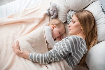 Top view of peaceful mother and cute child lying on double bed. They are sleeping together with...