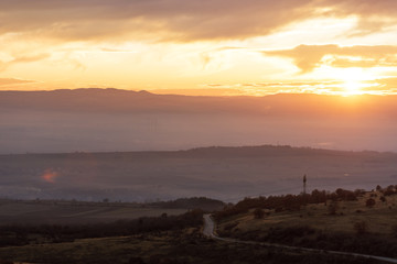 lonely road passing by mountains during a cloudy sunrise