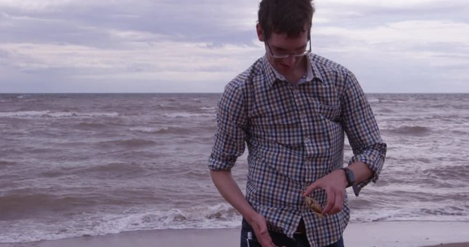 Young man plays with crab on beach towards camera