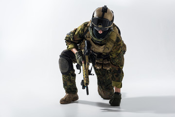 Portrait of tired soldier kneeling and leaning on arm while keeping modern weapon in hand. Military concept