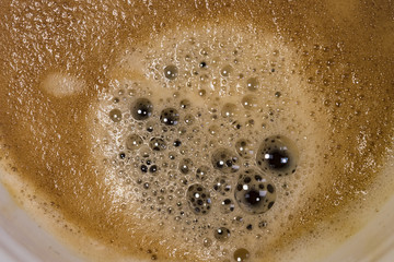 Fresh cup of Americano coffee seen close-up, showing the myriad of bubbles and thick froth. Part if the plan ceramic mug may be seen in this close-up image, taken in a well-known coffee franchise.