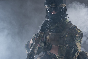 Portrait of serious soldier holding weapon in hands while standing in smoke. Occupation and danger...