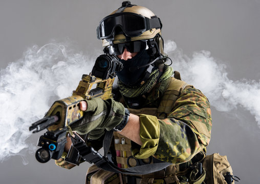 Portrait of serious soldier keeping assault rifle while standing in smoke. War concept