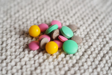 many multi-colored tablets and vitamin close-up on a knitted background