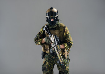 Portrait of stern male wearing military apparel while holding weapon in hands. Technology and war...
