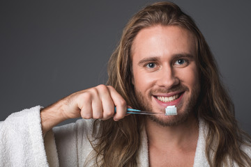 Healthy teeth. Portrait of smiling guy holding toothbrush in his hand. Isolated on grey background