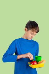 Boy holding lunch box with cup, bread, apple on green background