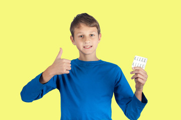 Boy in blue shirt shows finger up and pills. Isolated on yellow