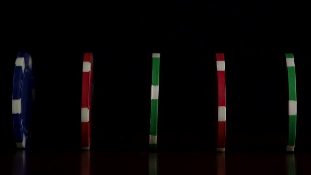 Poker chips stand in a row on a black background, a Domino effect. Playing poker chips are on the table, a symbol of casino