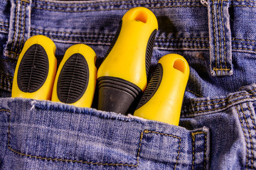 Yellow screwdrivers in a pocket of the blue jeans. Top view