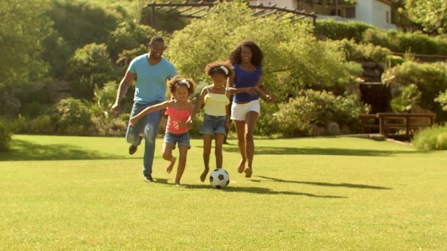 Family playing soccer in park running to camera