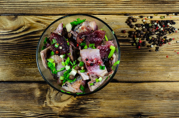 Herring with spices in glass bowl on wooden table. Top view