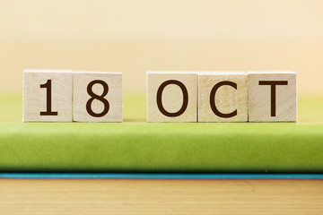 Wooden cube shape calendar for OCT 18 on green book, table.  