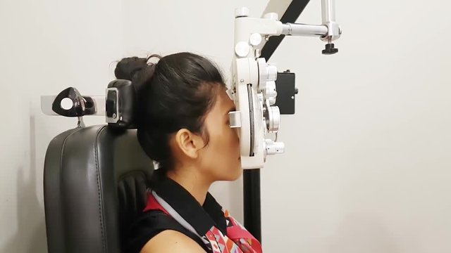 Young woman doing eye test with a phoropter instrument in an ophthalmologic clinic