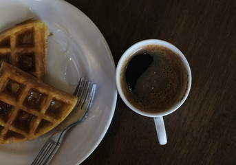 picture of black coffee in white glass with waffle topped with honey placed on the table at a coffee shop
