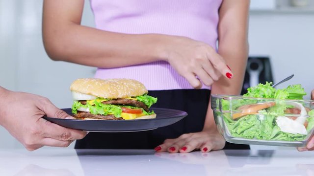 Dieting concept. Anonymous woman hands gesture rejecting a burger and taking a bowl of salad. Shot in 4k resolution
