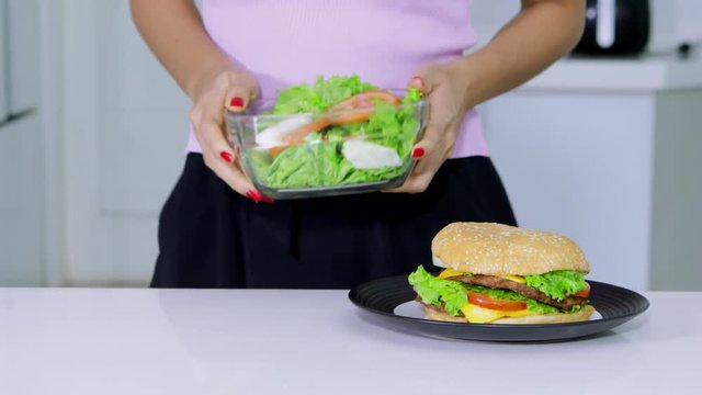 Dieting concept. Unknown woman choosing to take a bowl of salad than a plate of burger. Shot in 4k resolution