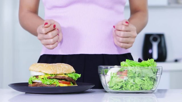 Dieting concept. Hands gesture of a doubtful unknown woman choosing vegetables salad or burger. Shot in 4k resolution