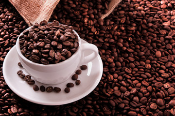 White coffee cup and saucer one single for espresso or capuccino on a background of scattered dark coffee beans with canvas burlap sack photo