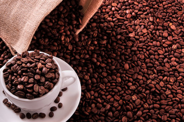 White coffee cup and saucer one single for espresso or capuccino on a background of scattered dark coffee beans with canvas bag sack photo