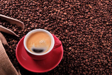 Red coffee cup and saucer one single for espresso americano or capuccino on a background of scattered dark coffee beans photo