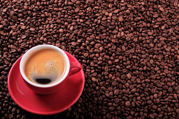 Red coffee cup and saucer one single for espresso americano or capuccino on a background of scattered dark coffee beans photo