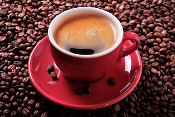 Red coffee cup and saucer one single for espresso americano or capuccino on a background of scattered dark coffee beans photo