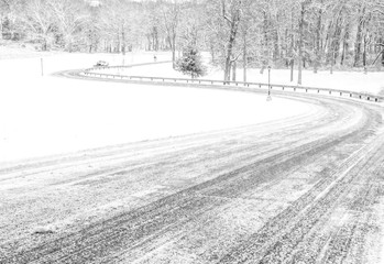Black and white winter rural scenery with the road covered in snow and forest on the background